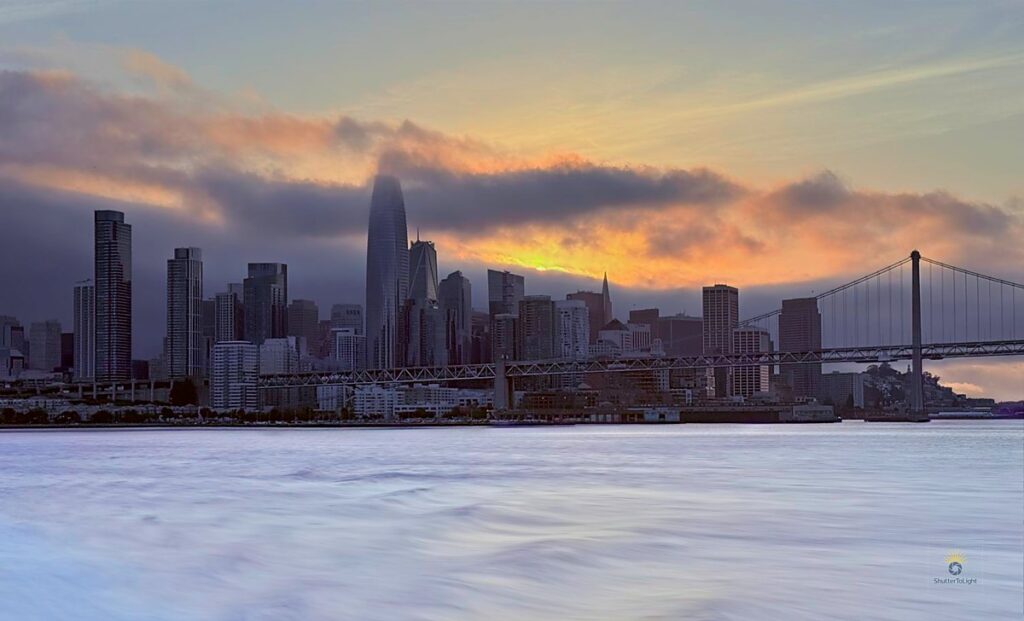 Skyline of San Francisco from boat at sunset with fog, bridge, and ripple trail.