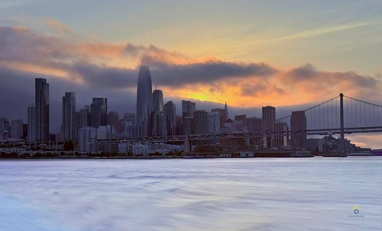 Skyline of San Francisco from boat at sunset with fog, bridge, and ripple trail.