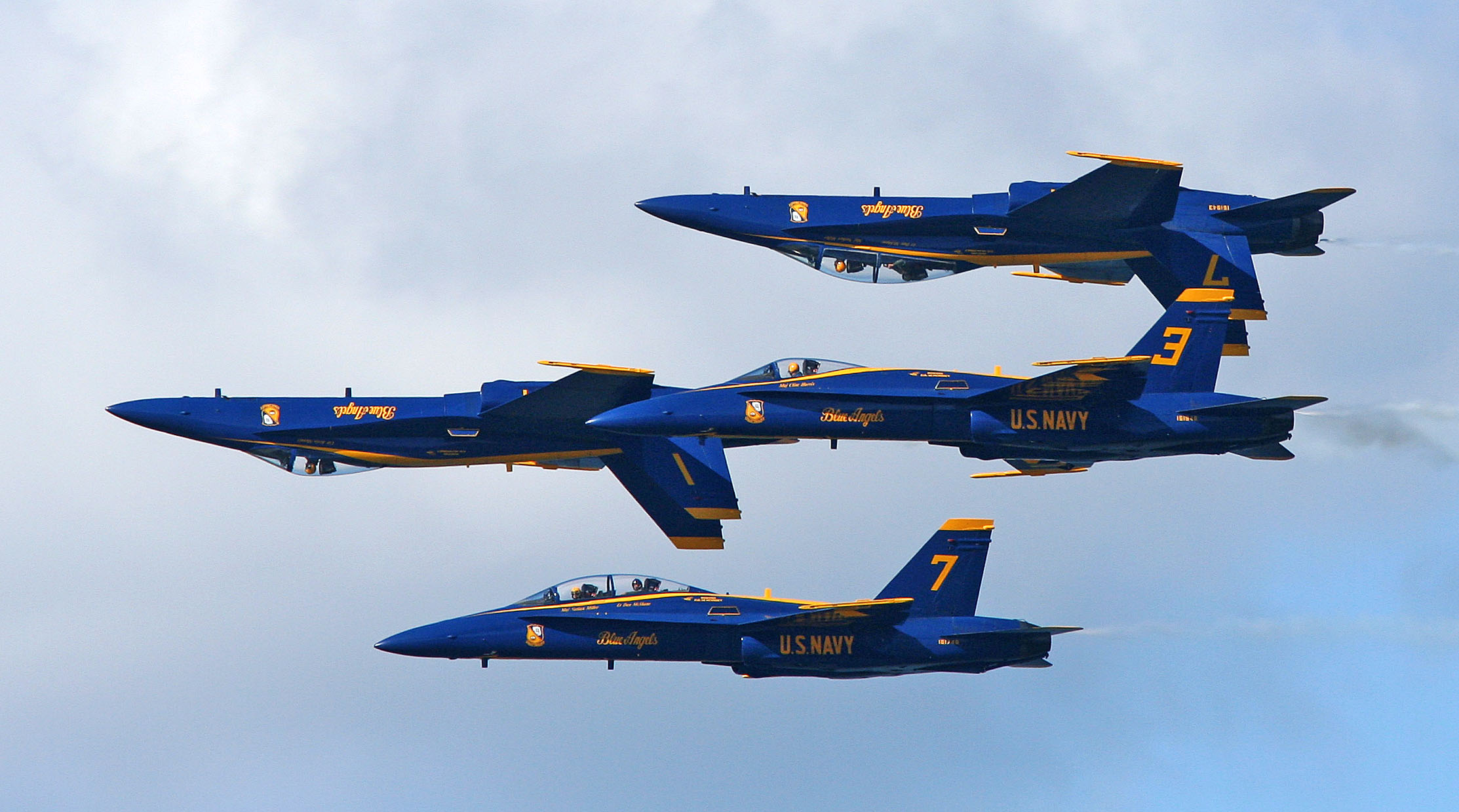 Three Blue Angels U.S. Navy fighter jets flying closely in a precise formation against a blue sky.