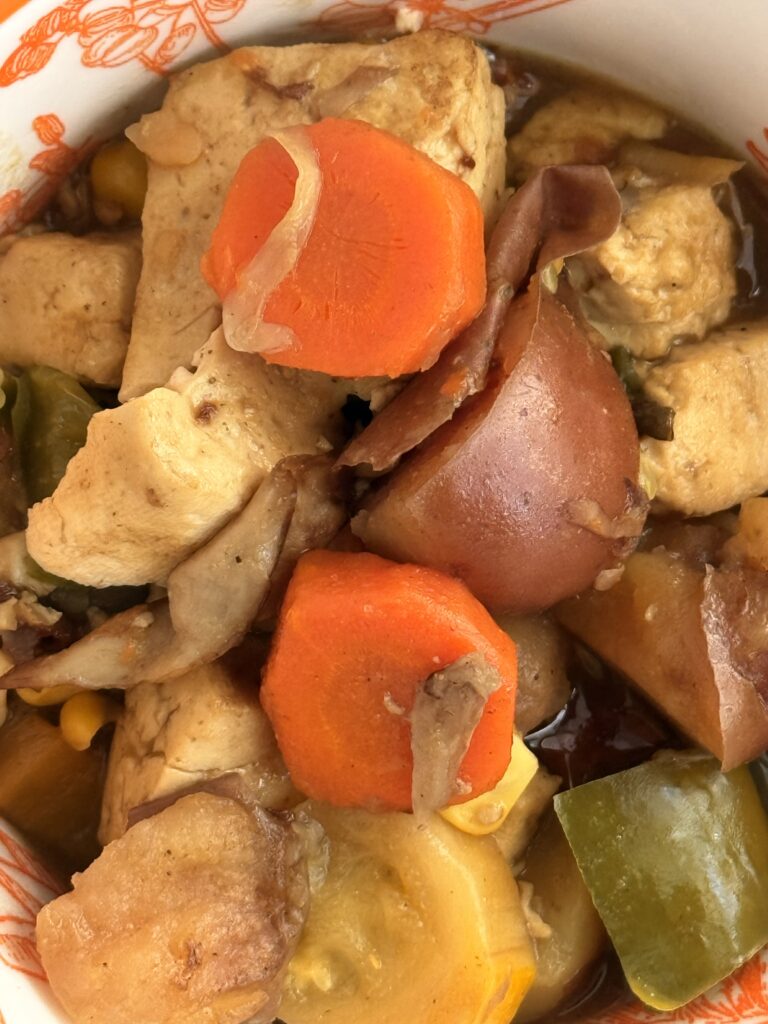 Close-up of a bowl filled with Japanese curry tofu stew, featuring chunks of tofu, carrots, red potatoes, green bell pepper, zucchini, and corn in a savory sauce.