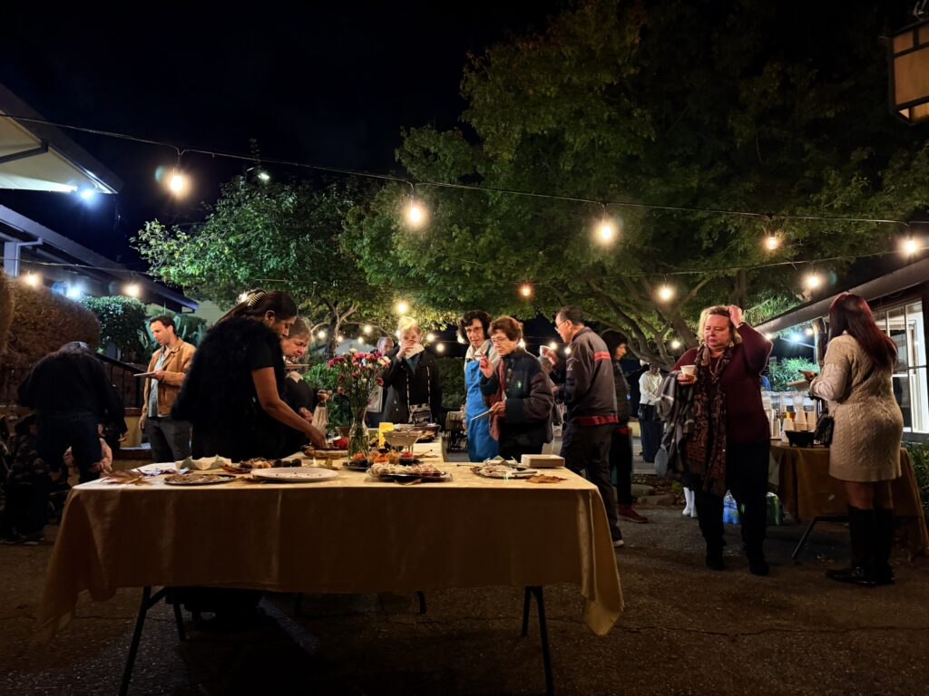 Evening outdoor reception at Olive-Hyde Art Center with guests mingling under string lights, enjoying refreshments and conversation around tables.