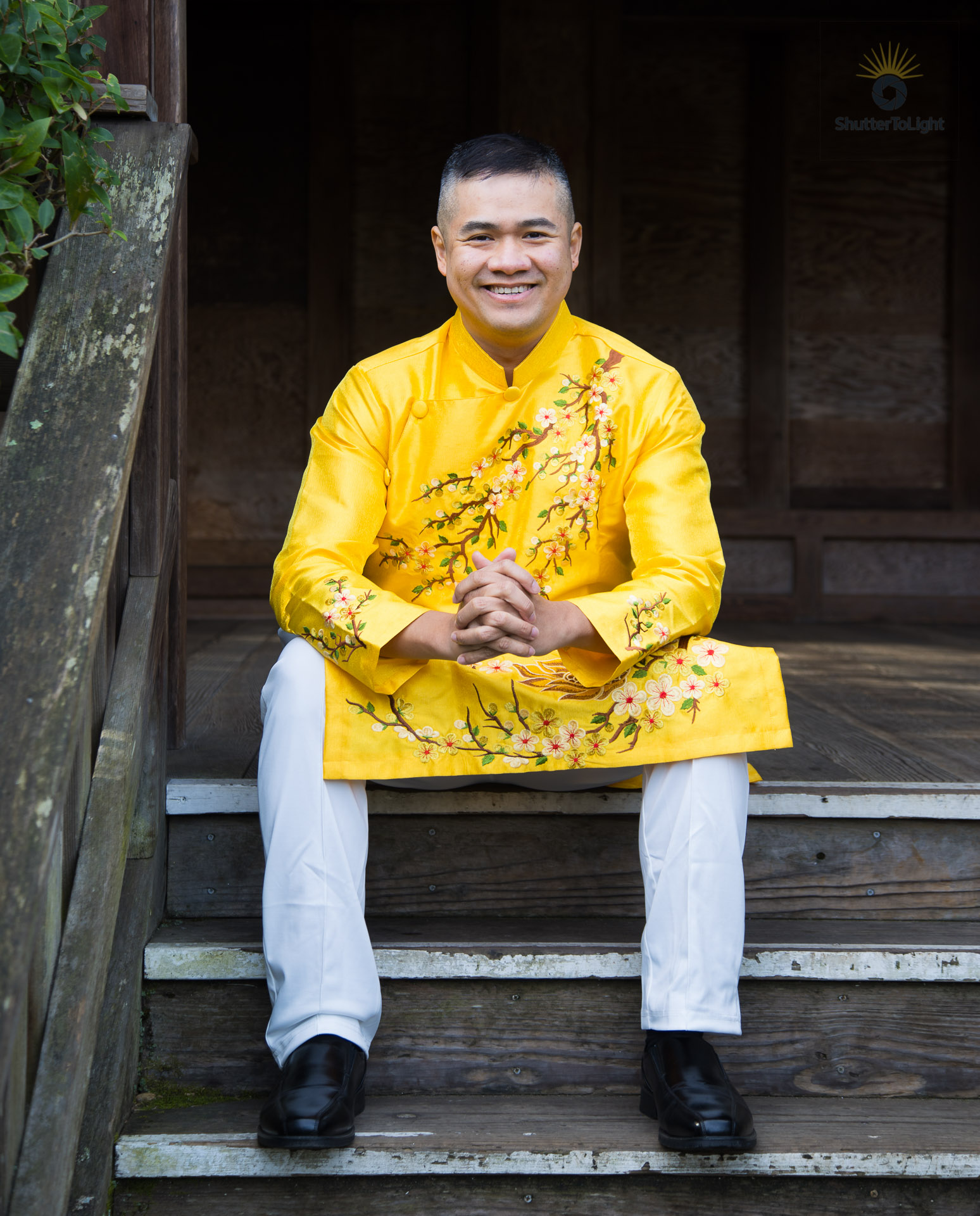 Uy Dinh in a golden Vietnamese áo dài embroidered with plum blossoms, seated on wooden steps at the Hayward Japanese Garden teahouse, calm expression and centered posture.